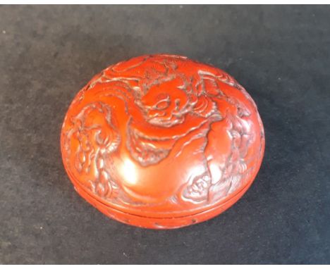 A 19thC Japanese carved red lacquer manju netsuke decorated with a pair of shishi in a sylvan setting.