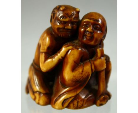 A JAPANESE CARVED AND STAINED IVORY NETSUKE of a crouching man and an oni, 4cm high.