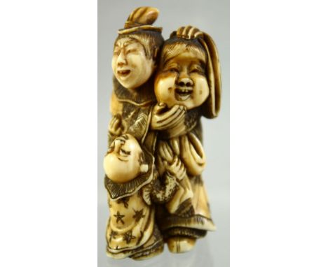 A JAPANESE CARVED IVORY NETSUKE of a man holding a mask, an inquisitive child at his feet, signed to the reverse, 5cm high.