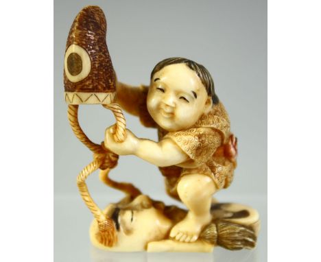 A GOOD SMALL JAPANESE CARVED IVORY OKIMONO of a child lifting a hat off of a noh mask, signed, 5.5cm high.