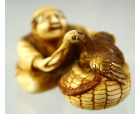 A JAPANESE CARVED IVORY NETSUKE of a seated man hand feeding a bird in a basket, signed to the base, 4.5cm wide.