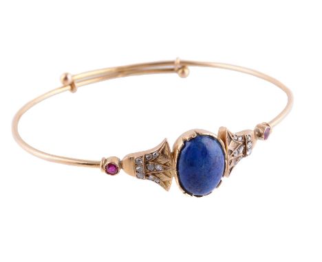 An Egyptian lapis lazuli, diamond and ruby bangle, the oval cabochon lapis lazuli between two lotus flower panels set with ro