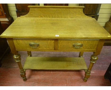 An early 20th Century oak side table having two drawers with brass drop handles to turned, cup and block supports with a narr