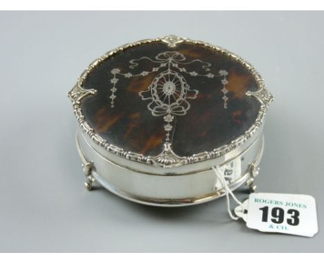 A circular silver ring box on three scrolled supports with fine silver and tortoiseshell lid inlaid with garlands and ribbons