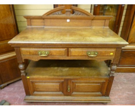 An Edwardian oak dumb waiter having two narrow top drawers to a centre shelf with two cupboards below and having turned side 