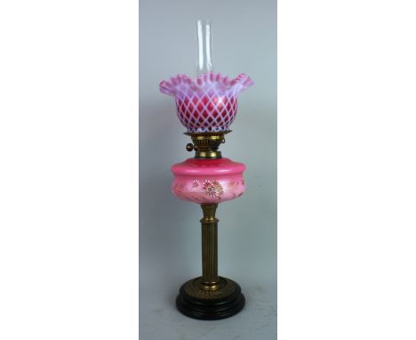 A Victorian style table oil lamp, with black glazed base supporting a reeded brass column, pink opaque glass reservoir enamel