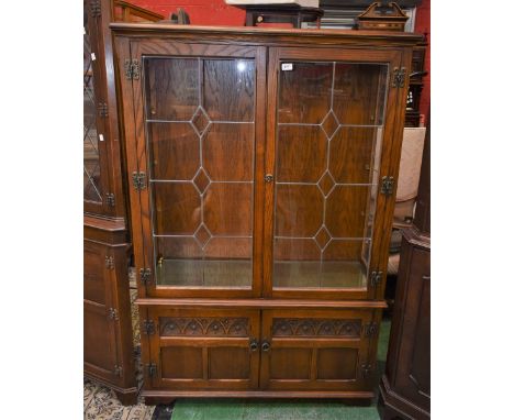 An Old Charm oak display cabinet model no.1918, two lead glazed doors enclosing shelving over two door cupboard, stile feet. 