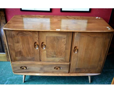 An Ercol elm sideboard, oversailing top, small cupboard over single drawer, adjacent large cupboard with cutlery drawer, spre