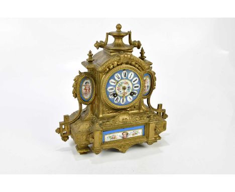 A late 19th century gilt metal French mantel clock with urn finial and porcelain panels, the porcelain dial set with Roman nu