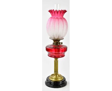 A Victorian oil lamp, the cranberry and clear fluted glass shade with wavy rim above the cranberry glass reservoir on a flute