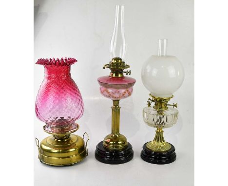 A brass oil lamp with a large cranberry glass shade, together with two further brass oil lamps, largest 68cm.Condition Report