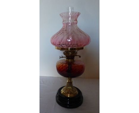 A tall Victorian oil lamp. Brass based with&nbsp;Cranberry and Amber glass. sat on a black glass plinth, 59 cm high