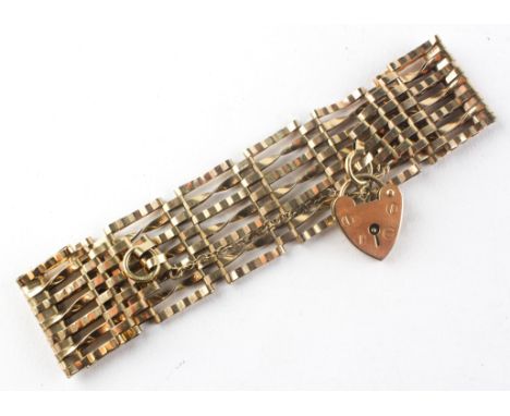 A yellow metal 23.0mm wide seven bar gate bracelet with padlock and fitted safety chain. Hallmarked 9ct gold. 15.9 grams