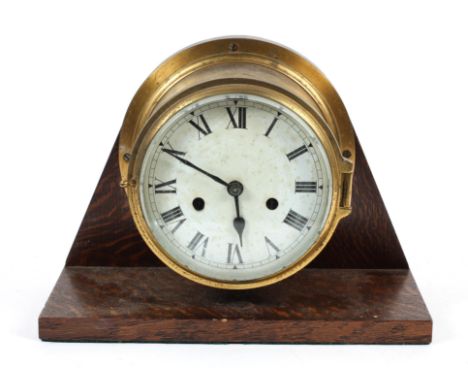 A brass ship's bulkhead clock on oak mount, early 20th century, with cylindrical brass case and white enamel dial with two wi