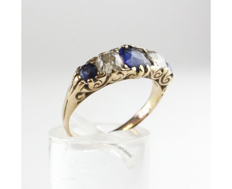 A yellow metal carved half hoop ring. Principally set with a cushion cut blue sapphire, flanked by an old European cut diamon