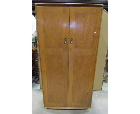 An Ercol medium elm wardrobe enclosed by a pair of full length rectangular panelled doors and raised on shepherds type castor