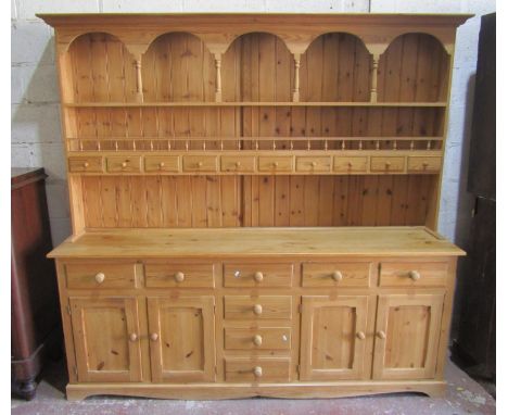 A large stripped pine kitchen dresser, the base enclosed by a T shaped arrangement of eight drawers, flanked by cupboards ben