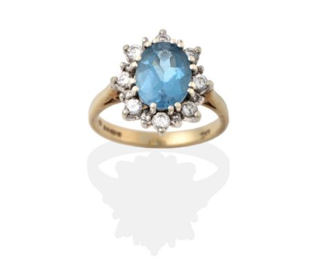 A 9 Carat Gold Blue Topaz and Diamond Cluster Ring, the oval cut blue topaz in a white double claw setting within a border of