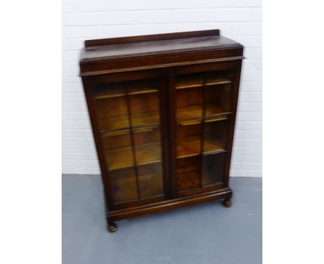 A 1930s oak ledgeback display case having astragal panel doors enclosing three adjustable shelves raised on bun feet (a/f) 92