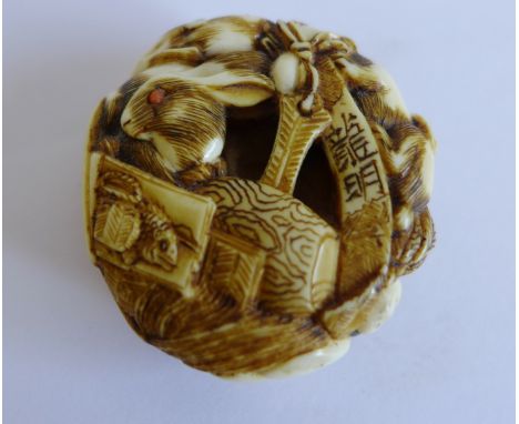 A Japanese ivory netsuke, the small circular pebble intricately carved with many hares having small coral eyes, fish, barrels