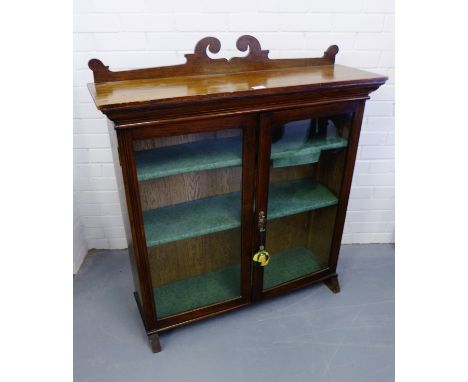 An Edwardian mahogany display cabinet having a scroll worked ledgeback over two glazed panel doors enclosing shelved interior