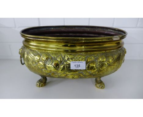 An oval floral embossed brass planter with lion mask handles to side and raised on hairy claw feet 