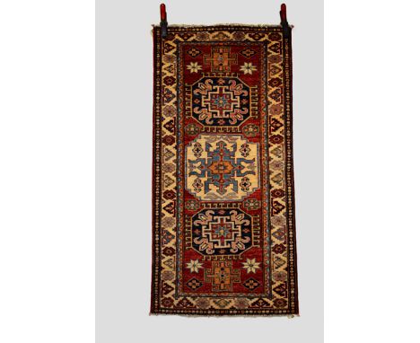 Caucasian design rug, Afghanistan, modern production, 4ft. 7in. X 2ft. 3in. 1.40m. X 0.69m. Dark blue and ivory medallions on