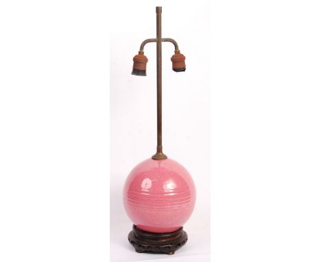 An unusual Chinese antique 19th Century pink glazed porcelain ball converted into a table lamp raised on a carved wooden socl