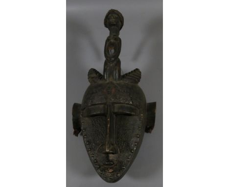An African Senufo carved wood farmers mask, having figural finial formed as a crouching naked tribes woman and with metal ado