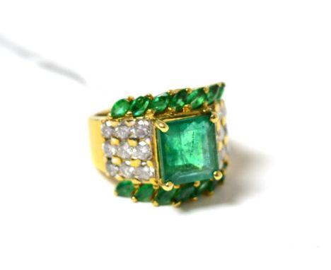 An emerald and diamond cluster ring, an emerald-cut emerald in yellow claw setting, flanked by round brilliant cut diamonds a