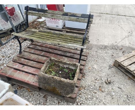 A WOODEN SLATTED GARDEN BENCH WITH CAST BENCH ENDS AND A RECONSTITUTED STONE PLANTER 