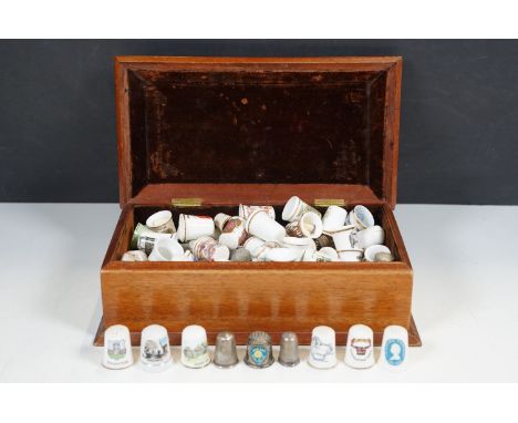 A collection of thimbles to include ceramic and metal examples contained within a wooden box. 