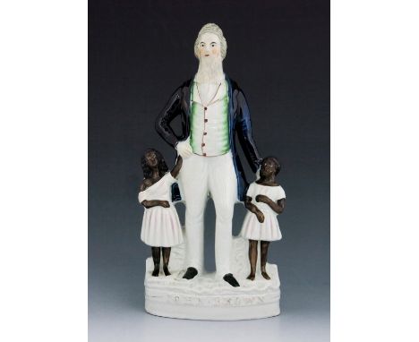 A Staffordshire figure of the Abolitionist John Brown, circa 1863, modelled standing between two slave children, wearing a bl