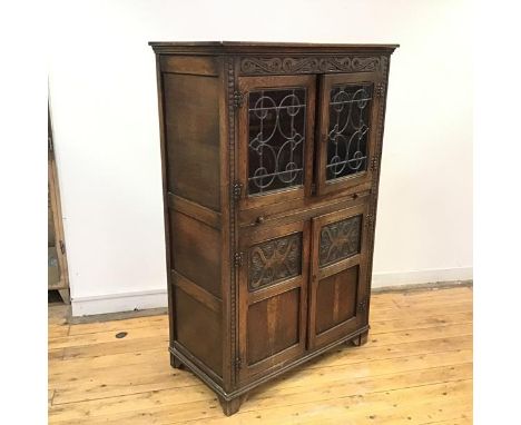 An Ercol style oak cabinet, in 17thc style, with a carved frieze above a pair of leaded glazed doors, enclosing a shelf above