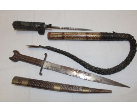 An Eastern-style dagger with double edged blade and carved wood hilt in brass mounted wood scabbard and an Indian hand whip, 