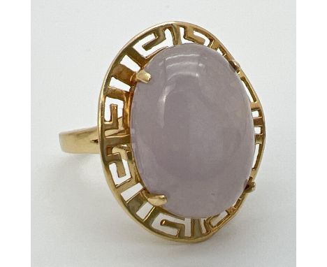 A 14K gold dress ring set with a large oval cabochon of lavender jade. In a Greek key pierced work mount with fluted edge. Ri