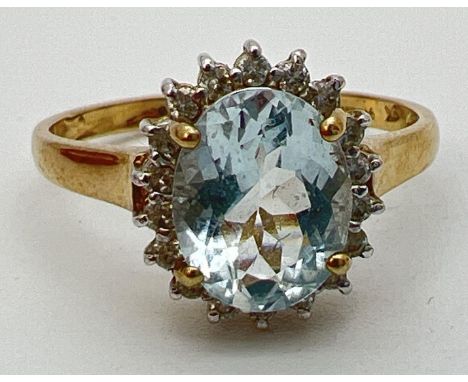 A 9ct gold aquamarine and diamond halo style dress ring. A central oval cut aquamarine (10mm x 8mm) surrounded by 18 small ro