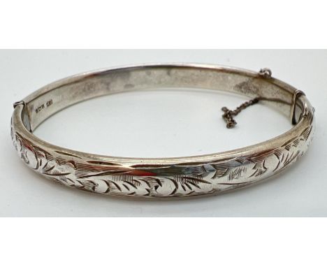 A vintage silver hinged bangle with half floral engraved decoration. Safety chain needs attention. Hallmarked Birmingham 1965