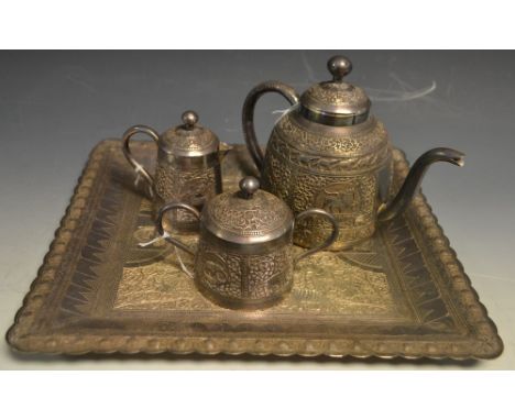 An Indian silver coloured metal three piece tea service on tray, comprising teapot, covered milk jug and sucrier, chased and 