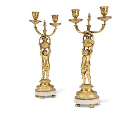 A pair of Restauration ormolu and white marble twin-branch candelabra, c.1820-30, each modelled as a putto with arms aloft su