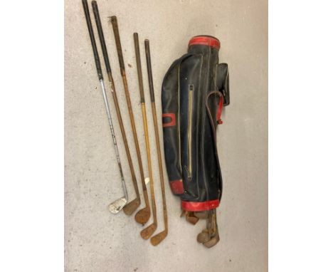 A black and red vintage golf club bag with a collection of vintage golf clubs in varying sizes and conditions, Mostly irons. 