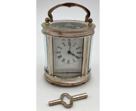 A small oval shaped carriage clock with glass panelled sides and top, enamelled face and roman numeral markers. Complete with