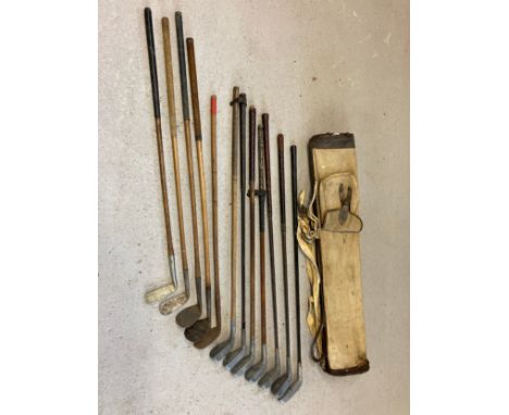 A vintage canvas and leather pencil golf club bag together with a collection of hickory handled golf clubs in varying conditi