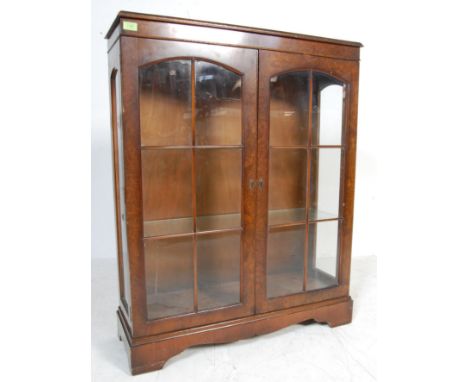A mid 20th century antique style walnut china display cabinet of a pedestal form with twin gaze doors, glass shelves raised o