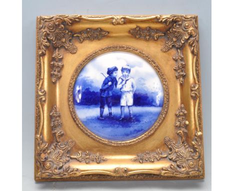 An early 20th century Edwardian blue and white ceramic plaque. The circular plaque depicting two boys set in a gild frame wit