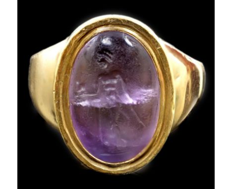 A Roman oval intaglio amethyst, carved with a figure with staff and pedestal, set in a later heavy gold ring mount, with a cl