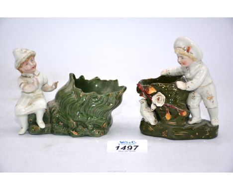 Two small ornaments of young children beside green tree trunk/vases; one with applied bird and flowers with glazed base stamp
