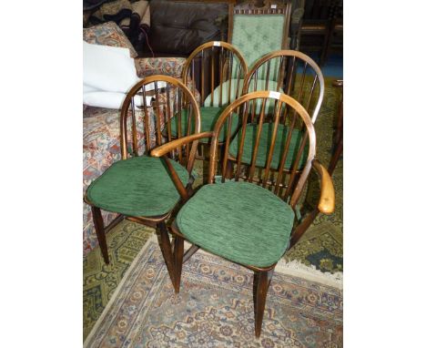 A set of four solid wood seated Ercol Dining Chairs having stick backs and green upholstered pad cushions, one being a carver