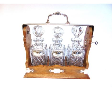 A SILVER PLATE MOUNTED WOODEN THREE DECANTER TANTALUS with silver wine labels for Sherry, Gin and Brandy, with key, 35cm long