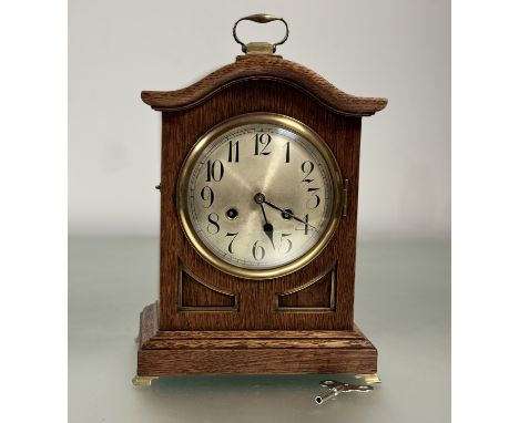 A late 19thc wooden oval mantle clock with Junghans B12 movement, silver clock face cased within domed glass cover with key. 